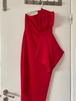 Röd oneshoulder klänning  - Snygg röd klänning med oneshoulder-design. Jag Den har en volangdetalj på axeln och sidan av klänningen. Klänningen har en asymmetrisk form och är knälång. 