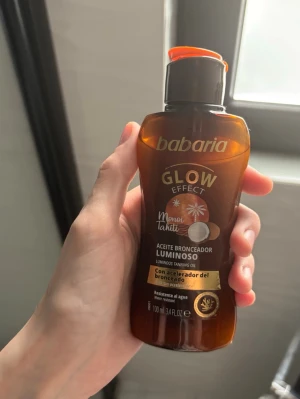 Babaria Glow Effect Bronzande Olja - Babaria Glow Effect Monoi Tahiti är en brun glasflaska med orange lock, innehållande luminös brun-utan-sol-olja. Oljan ger huden en glow-effekt och innehåller brun-utan-sol-accelerator. Flaskan rymmer 100 ml och är smidig att ta med. Perfekt för dig som vill ha extra lyster.
