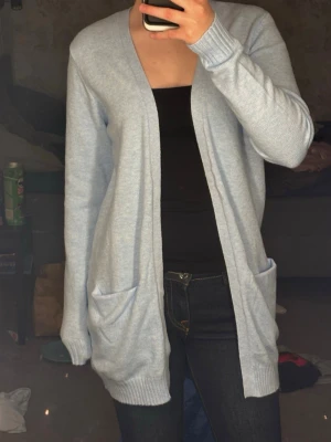 Ljusblå lång kofta, ljuslila, ny med prislapp - Mysig ljusblå och lila  lång kofta med två stora fickor framtill och ribbade muddar vid ärmslut och nederkant. Koftan har en öppen design utan knappar och är perfekt att slänga över en topp. Materialet är mjukt och stretchigt. Från märket VILA   ”Viral open knot cardigan” i färgerna orchid och blue☺️ nypris 365kr