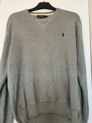 Polo Ralph Lauren stickad tröja grå – klassisk – M – fint skick - Säljer en grå Polo Ralph Lauren tröja i storlek M.  Väldigt fint skick.  Klassisk modell som passar till allt.  Nypris runt 1000+ kr.  Säljes billigt vid snabb affär.