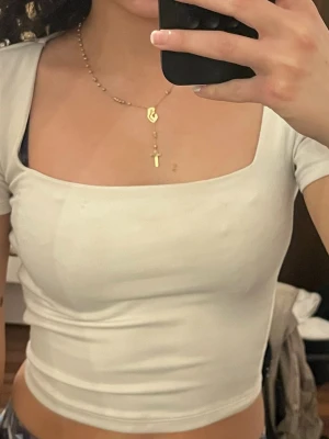 Vit croppad topp med fyrkantig ringning - Säljer en vit croppad topp med fyrkantig ringning och korta ärmar. Toppen har en tight passform och är perfekt att styla med höga jeans eller kjol. Enkel och stilren design utan mönster eller detaljer.