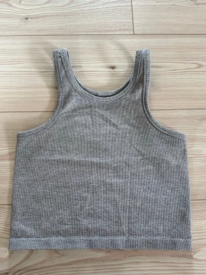 Grå ribbad linnetopp - Säljer en enkel och stilren grå ribbad linnetopp från HM. Toppen är ärmlös och har en croppad passform som passar perfekt till höga jeans eller kjol. Materialet är mjukt och stretchigt för en bekväm känsla.