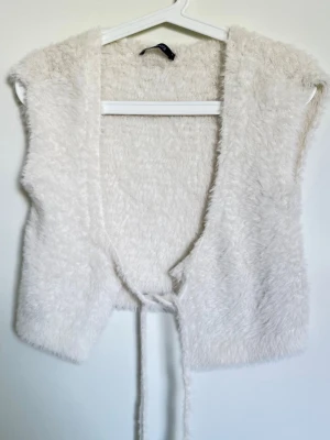 Vit fluffig pälsväst från Gina Tricot - Supersöt vit pälsväst från Gina Tricot i storlek S. Västen är gjord i mjukt, fluffigt fuskpälsmaterial och har knytband framtill✨