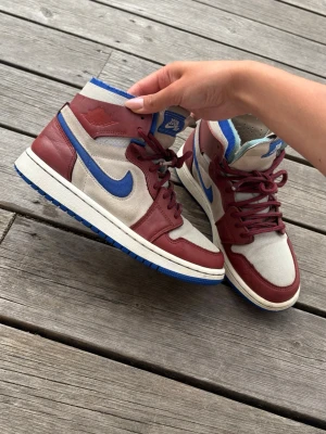 Nike Air Jordan 1 High - Snygga Nike Air Jordan 1 High sneakers i rött och vitt med blå detaljer. Skorna har klassisk hög siluett. Super mjuka och bekväma!