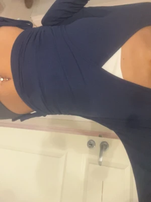Mörkblå omlottopp med v-ringning - Snygg mörkblå omlottopp med v-ringning och långa ärmar. Toppen har croppad passform och knyt i sidan för en trendig look. Perfekt att styla med höga jeans eller kjol. Materialet känns mjukt och stretchigt.
