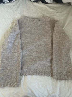 Beige stickad tröja med rund hals - Mysig beige stickad tröja med rund hals och långa ärmar. Tröjan har ribbstickade muddar vid ärmslut och nederkant. Perfekt för lager på lager och enkel att matcha med olika outfits.
