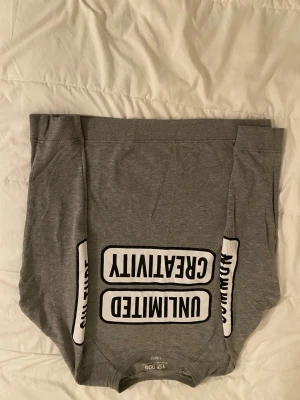 Grå sweatshirt med tryck från 157 - Grå sweatshirt från 157 med svartvitt tryck på bröstet där det står 'UNLIMITED CREATIVITY'. Tröjan har rund halsringning och långa ärmar. Perfekt för en avslappnad och trendig stil.