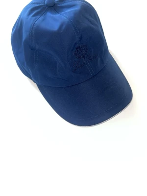 Mörkblå keps från Loro Piana - Snygg mörkblå keps från Loro Piana med broderad logga framtill. Klassisk böjd skärm. Tillverkad i ett mjukt tyg som känns bekvämt på huvudet. Perfekt accessoar för en avslappnad och sportig stil.