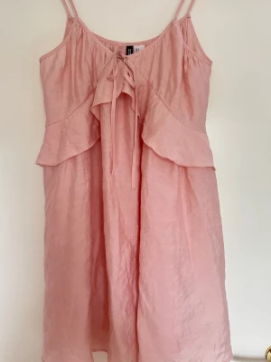 Gullig klänning  - Söt rosa kortklänning från H&M Divided med tunna axelband, och knyt framtill. Klänningen har volangdetaljer vid bysten och är tillverkad i ett lätt, glansigt material som ger en luftig känsla. Använd 3 gånger