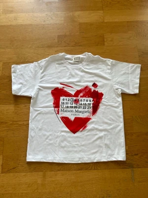 Maison Margiela vit t-shirt med rött hjärta - Vit oversized t-shirt från Maison Margiela i storlek S men passar lika bra på M. Perfekt till sommaren för en clean outifit. Hör av er vid intresse.