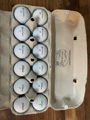 12 st titleist och taylormade bollar - Säljer en äggkartong fylld med golfbollar från Titleist och TaylorMade. Bollarna är vita och har olika nummer och markeringar. Perfekt för dig som vill fylla på golfväskan med extra bollar till nästa runda. 6 bollar från varje märke. Vissa bollar kan ha repor och färger men inget som förstör spelet enligt mig