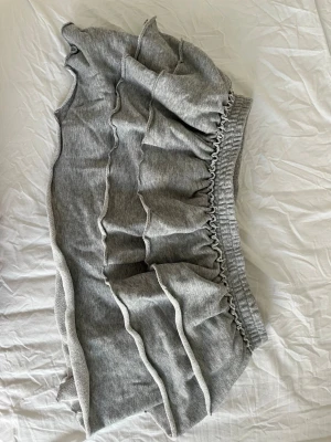 Grå volangkjol med resårmidja i mjukismaterial från Monki  - Snygg grå kortkjol med flera volanger och bred resår i midjan. Kjolen är gjord i mjukt bomullsmaterial och har en avslappnad, bekväm passform. Perfekt för dig som gillar en sportig men ändå söt stil.
