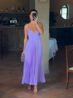 Ljuslila plisserad långklänning - Säljer en elegant ljuslila långklänning med smala axelband och v-ringning. Klänningen har plisserad kjol och är ärmlös, vilket ger en luftig och stilren look. Perfekt för speciella tillfällen och sommarens event.