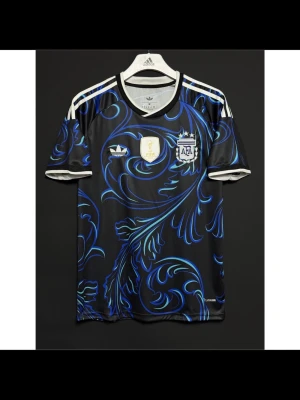 Argentina Adidas fotbollströja svart/blå - Snygg svart fotbollströja från Adidas med blått och turkost mönster, officiella Argentina-märket och FIFA-märke på bröstet. Klassiska vita Adidas-ränder på axlarna och rund hals. Perfekt för dig som älskar fotboll och vill sticka ut på planen.