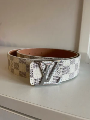 Vit och beige bälte - Snyggt bälte  i vitt och beige med klassiskt rutigt mönster och Bältet har en exklusiv känsla och passar perfekt till jeans eller byxor för en trendig look.