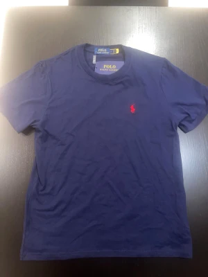 Marinblå t-shirt från Polo Ralph Lauren - Snygg marinblå t-shirt från Polo Ralph Lauren med klassisk röd broderad logga på bröstet. T-shirten har rund halsringning och korta ärmar. Tillverkad i mjuk bomull för skön känsla och stilren look.