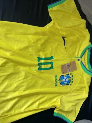 Gul Brasilien fotbollströja Nike - Säljer en gul Brasilien fotbollströja från Nike med nummer 10 och CBF-emblemet på bröstet. Tröjan har gröna och blå detaljer vid krage och ärmslut samt Nike-logga på bröstet. Perfekt för dig som älskar fotboll och vill stötta Brasilien.