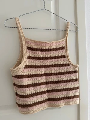 Randig virkad linnetopp i beige och brun - Superfin virkad linnetopp med breda axelband i beige, ljusrosa och bruna ränder. Toppen har en croppad passform och är perfekt för sommaren. Mjuk och skön med handgjord känsla, passar till både jeans och kjol.