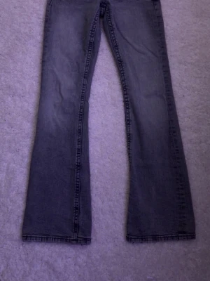 Grå bootcut jeans Gina Tricot  - Säljer ett par grå bootcut jeans från Gina Tricot med snygga sömmar och detaljerade bakfickor. Jeansen har en klassisk femficksmodell och är tillverkade i denim med lätt tvättad look. Perfekta för dig som gillar en avslappnad men ändå trendig stil. Knappt använda skriv vid intresse skickar samma dag eller dagen efter!