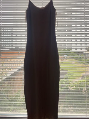Beige långklänning med smala axelband - En stilren beige långklänning med smala axelband och rak passform. Klänningen har en enkel design utan mönster eller detaljer och är perfekt för en minimalistisk look. Materialet ser ut att vara mjukt och följsamt, vilket ger en snygg siluett. Dene jätte ljus biegsh