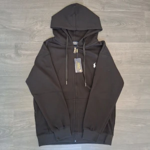Svart hoodie från Polo Ralph Lauren - Svart hoodie med dragkedja från Polo Ralph Lauren. Klassisk design med huva och justerbara snören, samt fickor framtill. Ikoniska vita Polo-loggan broderad på bröstet. Tillverkad i mjukt bomullsmaterial för en skön och avslappnad look. Tagg och påse ingår. Storlek L men passar M bättre.