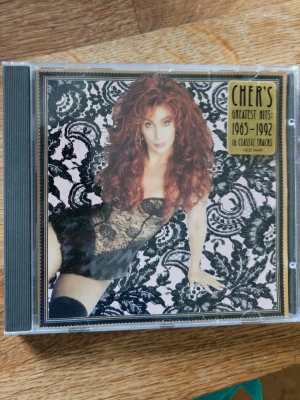 CHER'S Greatest Hits 1965-1992 CD - CD med CHER'S Greatest Hits 1965-1992. Omslaget har svart spetsmönster och bild på Cher. Innehåller 16 klassiska låtar, bland annat 'If I Could Turn Back Time' och 'Bang-Bang'. Perfekt för dig som gillar pop och klassiska hits.