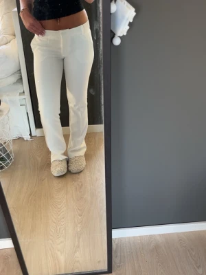 Vita bootcut kostymbyxor - Snygga vita kostymbyxor med bootcut passform och låg midja. Byxorna har bälteshällor och diskreta fickor fram. Perfekta för en clean och stilren look. Materialet ser ut att vara ett mjukt tyg med lite stretch.