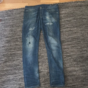 Mörkblåa Dondup George Jeans - Säljer ett par blå jeans med coola slitningar, hål och färgstänk för en riktigt avslappnad streetlook. Jeansen har fem fickor, normal midja och raka ben. Perfekta för dig som gillar en trendig och avslappnad stil.