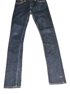 Mörkblå jeans från Nudie Jeans - Snygga mörkblå jeans från Nudie Jeans med raka ben och klassisk femficksmodell. Jeansen har kontrastsömmar och ikonisk brodyr på bakfickorna. Tillverkade i slitstark denim av bomull.