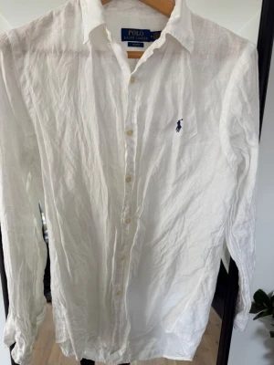 Vit linneskjorta Polo Ralph Lauren - Klassisk vit skjorta från Polo Ralph Lauren i linne med blå broderad logga på bröstet. Slim fit-modell med långa ärmar och knappar framtill. Perfekt för en clean och stilren look.