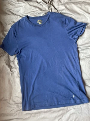 Blå t-shirt från Polo Ralph Lauren - Säljer en stilren blå t-shirt från Polo Ralph Lauren. T-shirten har en väldigt slim fit passform, rund halsringning och den ikoniska lilla loggan broderad nertill. Perfekt för en clean och enkel look. MODELLEN ÄR 181 CM