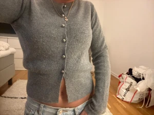 Grå ribbstickad kofta med pärlknappar - Snygg grå ribbstickad kofta med långa ärmar och pärlknappar framtill. Kortare modell som passar perfekt till jeans eller kjol. Mjuk och skön kvalitet, enkel att styla för en trendig look.