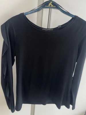 Svart långärmad topp med volang Esprit - Stilren svart långärmad topp med rund halsringning och volangdetaljer längs ärmarna. Perfekt att matcha med både jeans och kjol för en trendig look. Mjuk och bekväm, passar till många olika outfits.