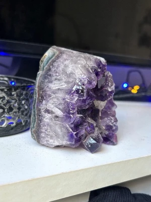Ametistkluster kristall dekor - Säljer ett snyggt ametistkluster med lila kristallspetsar och naturlig rå baksida. Perfekt som inredningsdetalj eller för kristallsamling. Stenen har en blandning av djupa lila och ljusare toner, med tydliga kristallformationer och naturliga kanter.