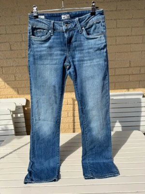Blå bootcut Pepe jeans 25/32 - Snygga blå bootcut jeans med klassisk femficksdesign och slitna detaljer. Jeansen har låg midja & dragkedjegylf. 25/32