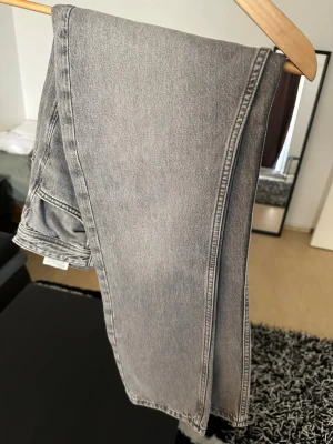 Grå raka jeans från Jack&Jones - Snygga grå jeans från Jack&Jones med rak passform och klassisk femficksdesign. Jeansen har en ljusgrå tvätt och är tillverkade i bomull. Perfekta för en avslappnad och trendig look.