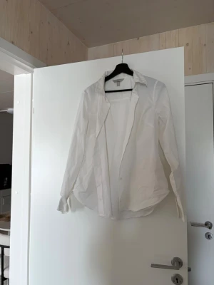 Vit klassisk skjorta från H&M - Vit skjorta i klassisk modell från H&M. Skjortan har krage, långa ärmar och knappar framtill. Tillverkad i bomull för en skön och luftig känsla. Perfekt att styla med jeans eller kostymbyxor.