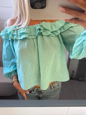 Mintgrön offshoulder blus med volang - Superfin mintgrön blus i bomull med offshoulder-modell och bred volang runt hela halsen. Långa ärmar med resår vid ärmslut ger en avslappnad och luftig känsla. Perfekt för dig som gillar en romantisk och trendig stil.
