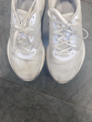 Vita Adidas sneakers med mesh - Snygga vita sneakers från Adidas med klassisk design. Skorna har ovandel i mesh för bra andningsförmåga och detaljer i syntet. Perfekta för en sportig och stilren look. Lågt skaft och snörning framtill.