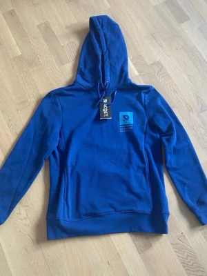Blå hoodie från RACQET med tryck - Blå hoodie från RACQET, helt ny med lappar kvar. Storlek S