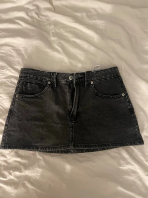 Svart jeanskjol  - Snygg svart kort jeanskjol med klassiska fem fickor och knappstängning framtill. Kjolen har en rak passform och är tillverkad i ett robust denimtyg. Perfekt att matcha med en t-shirt eller hoodie för en cool vardagslook. Det är även innershorts🥰helt nya