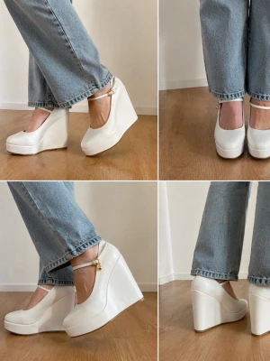 Vita platåpumps med rem - Säljer ett par vita pumps med hög platå och kilklack. Skorna har en rund tå och en elegant rem med guldfärgad detalj runt ankeln. Materialet ser ut att vara syntetiskt och de har en modern, chunky design som sticker ut.