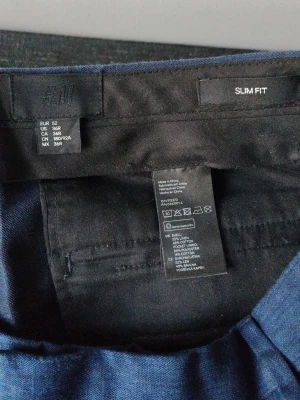 Blå slim fit chinos från H&M - Snygga blå slim fit chinos kostymbyxor från H&M i storlek 52 Slim (36R. Jeansen är tillverkade i en bomullsblandning med lite stretch för extra komfort. Perfekta för dig som gillar en smalare passform och stilren look.
