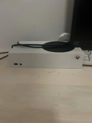 Xbox Series S vit spelkonsol - Säljer en Xbox Series S spelkonsol i vit färg med rund svart ventilationsyta på ovansidan. Konsolen har en kompakt och rektangulär design, tillverkad i plast. Perfekt för gaming och digitala spelupplevelser.