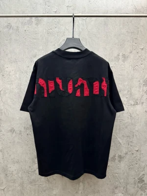 Svart t-shirt med röd textdetalj - Cool svart t-shirt med stora röda bokstäver i ett unikt mönster på ryggen. T-shirten har en klassisk passform och är kortärmad, perfekt för en avslappnad streetwear-look.