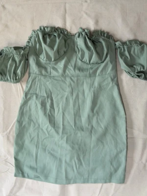 Ljusgrön offshoulder kortklänning - Trendig ljusgrön kortklänning med offshoulder och puffiga ärmar. Klänningen har rynkade detaljer upptill och markerad byst. Tillverkad i ett mjukt material som känns bekvämt mot huden. 