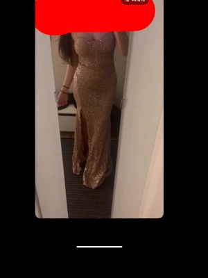 Champagnefärgad långklänning Fashion Nova - Helt oanvänd klänning, köpte den till balen men hittade en annan. Snygg långklänning från Fashion Nova i champagnefärg med glittrigt mönster och hög slits framtill. Klänningen har figurnära passform och är ärmlös, perfekt för speciella tillfällen. Materialet är glittrigt och ger en lyxig känsla.💕