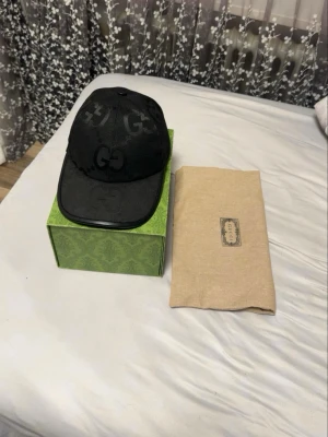 Svart keps från Gucci med GG-mönster - Säljer en svart keps från Gucci med klassiskt GG-monogram över hela kepsen. Kepsen har böjd skärm och är tillverkad i mesh och tyg, vilket ger en snygg och modern look. Perfekt accessoar för att lyfta din outfit. Äkta Keps kom privat