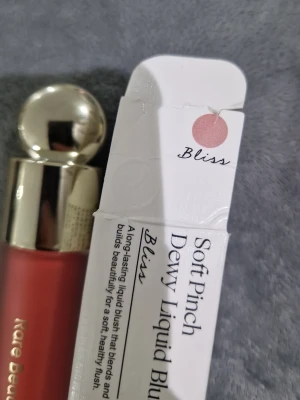 Rare Beauty Soft Pinch Dewy Liquid Blush - Rare Beauty Soft Pinch Dewy Liquid Blush i nyansen Bliss. Flytande rouge med dewy finish i en mjuk, persikorosa ton. Kommer i en stilren glasflaska med guldig applikator. Perfekt för att ge kinderna en fräsch och naturlig glow.