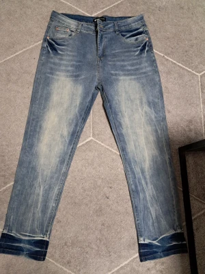 Blå jeans  - Säljer ett par blå jeans från Purple Brand med snyggt slitna detaljer och ljusa partier framtill. Jeansen har klassisk femficksdesign, raka ben och uppvikta benslut. Perfekta för dig som gillar en avslappnad och trendig stil.